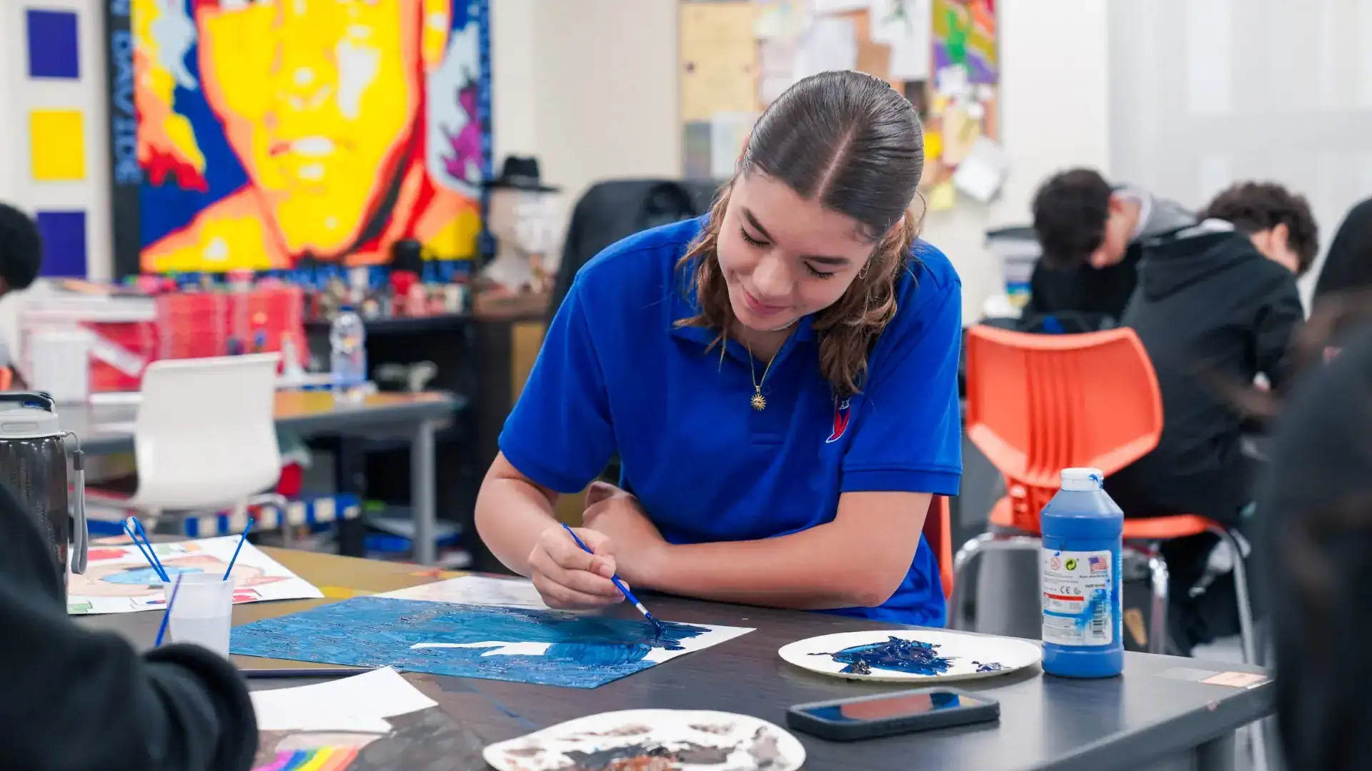 An AISJ student painting at a table in the visual arts studio
