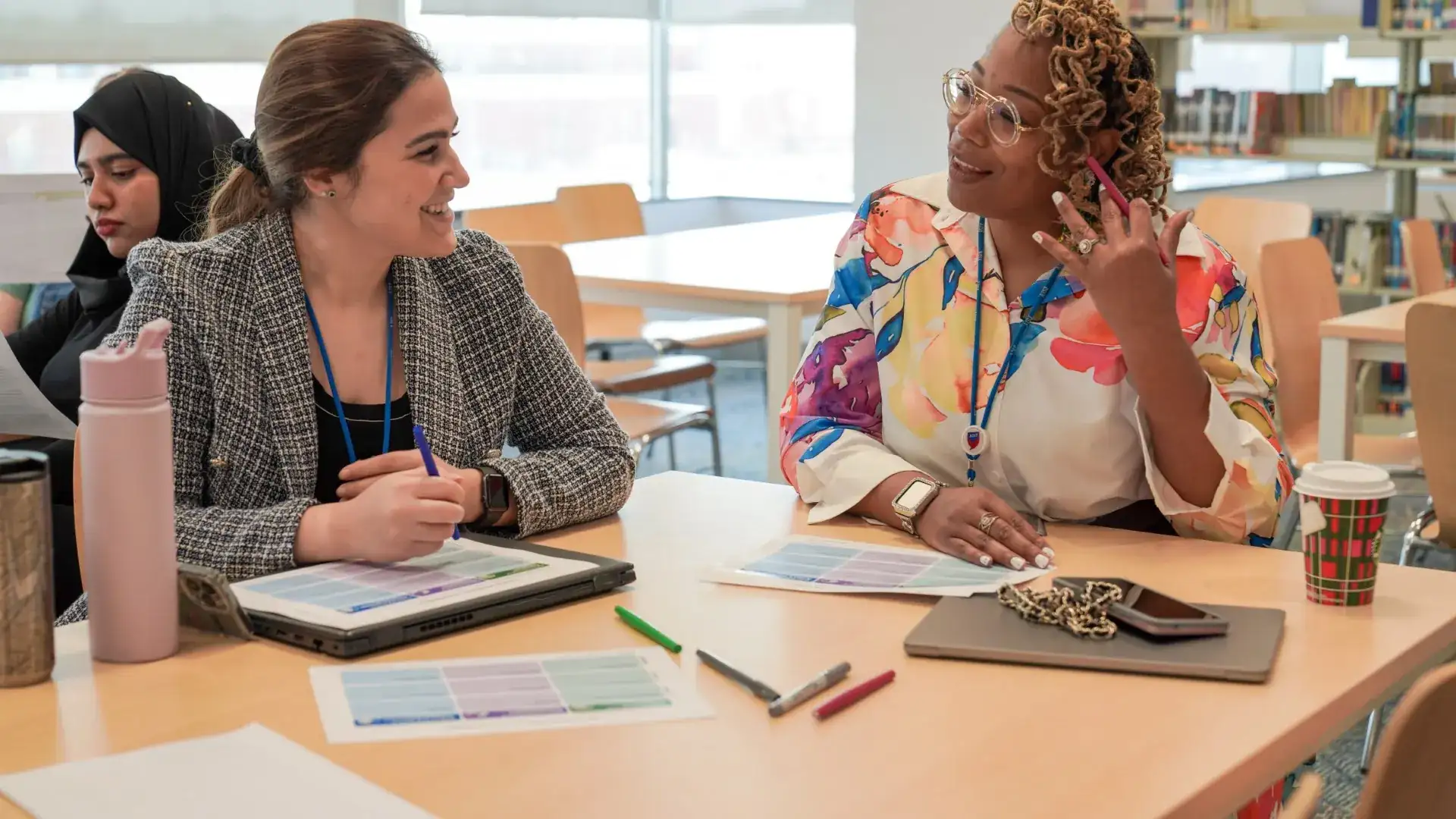 AISJ staff members smile and talk together at a table in the library.
