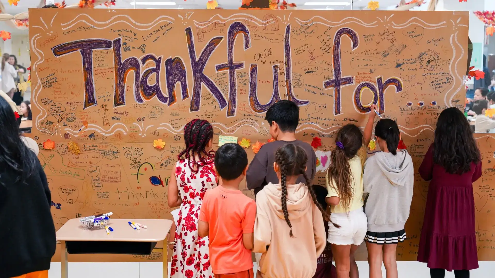 Students adding notes to a large handwritten "Thankful for" paper wall at AISJ