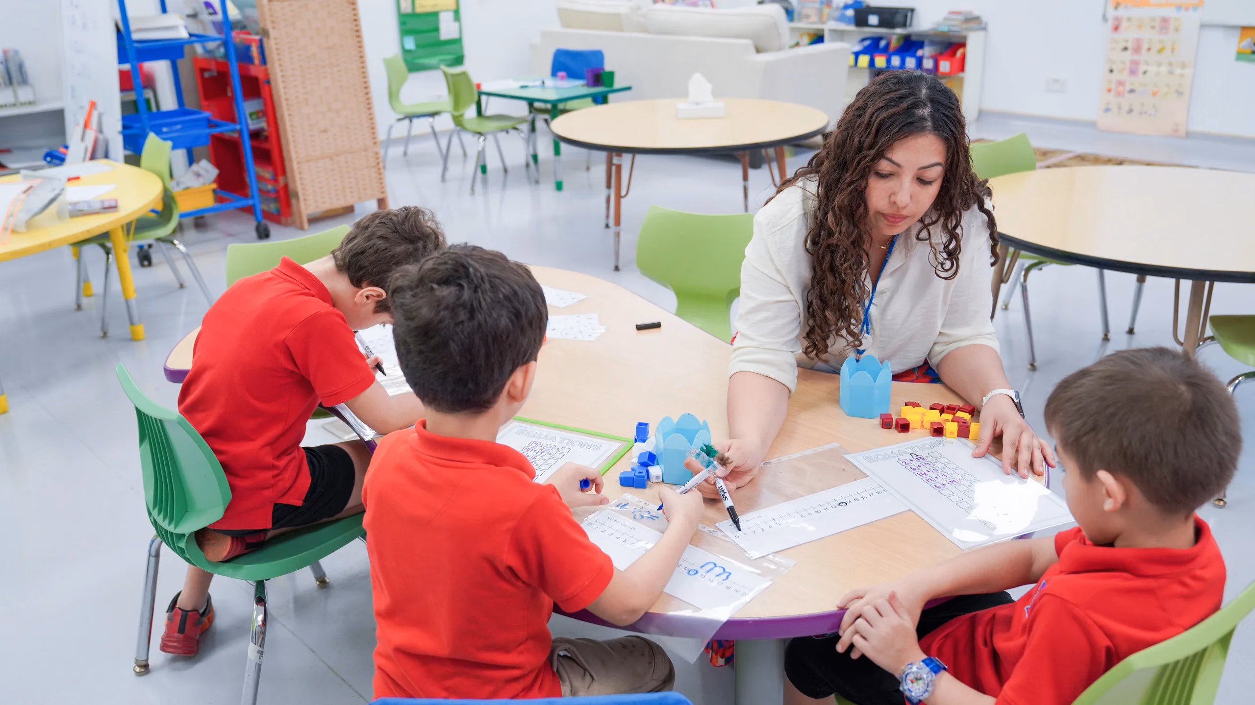 أطفال مرحلة الطفولة المبكرة في AISJ يعملون مع معلمتهم حول طاولة الصف