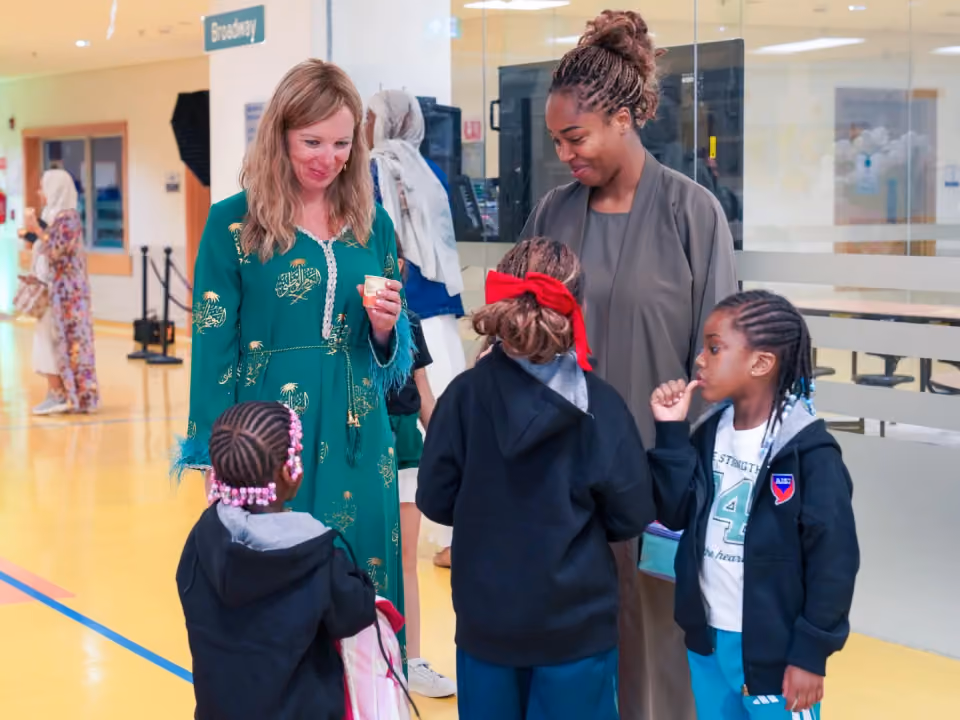 An AISJ teacher welcoming students and family members in the school hallway