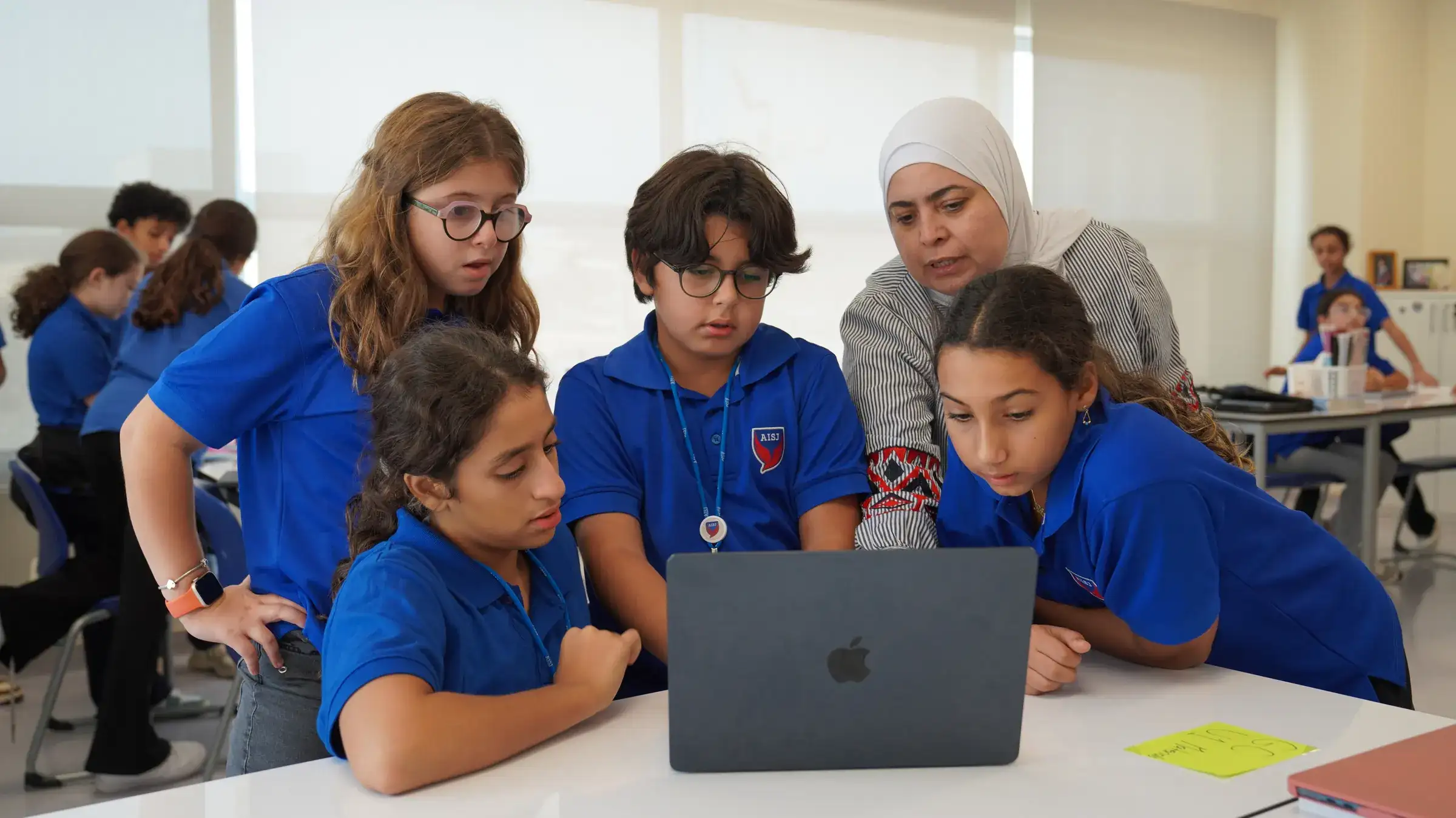 معلمة ومجموعة من طلاب المرحلة المتوسطة يجتمعون حول حاسوب محمول للعمل معاً على حل مسألة.
