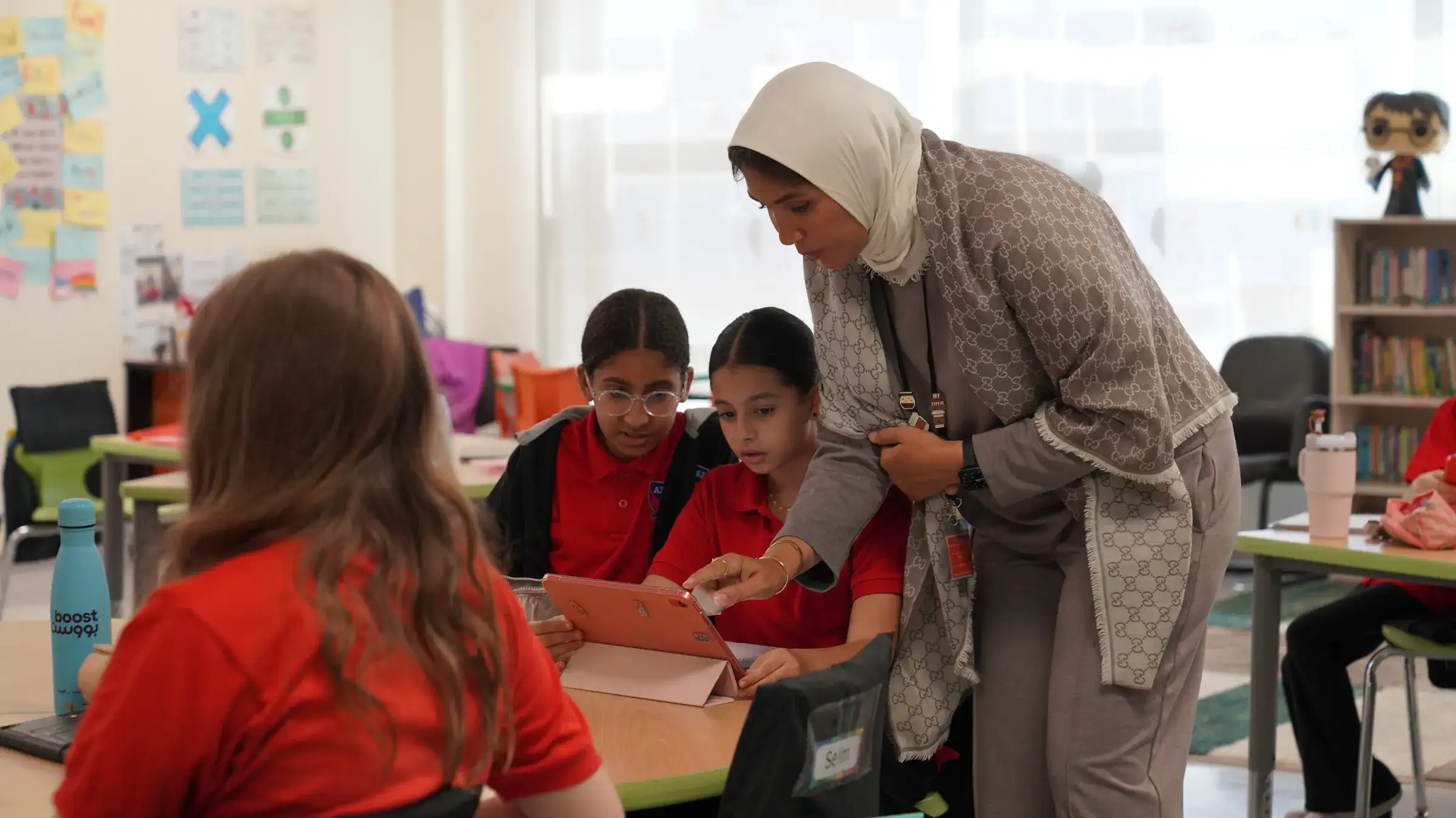 A teacher guiding a small group of elementary students on a tablet.