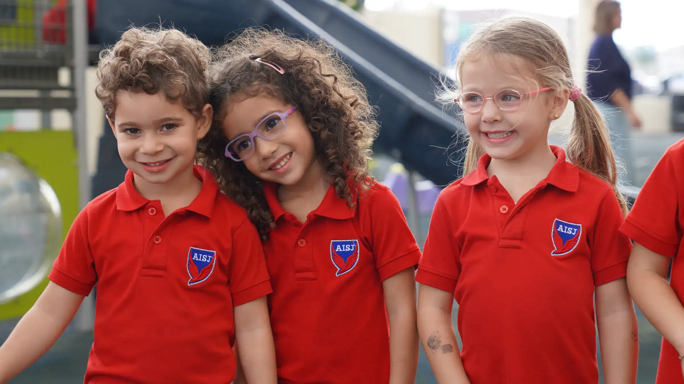 Three young AISJ students in red crest polo shirts at the playground.